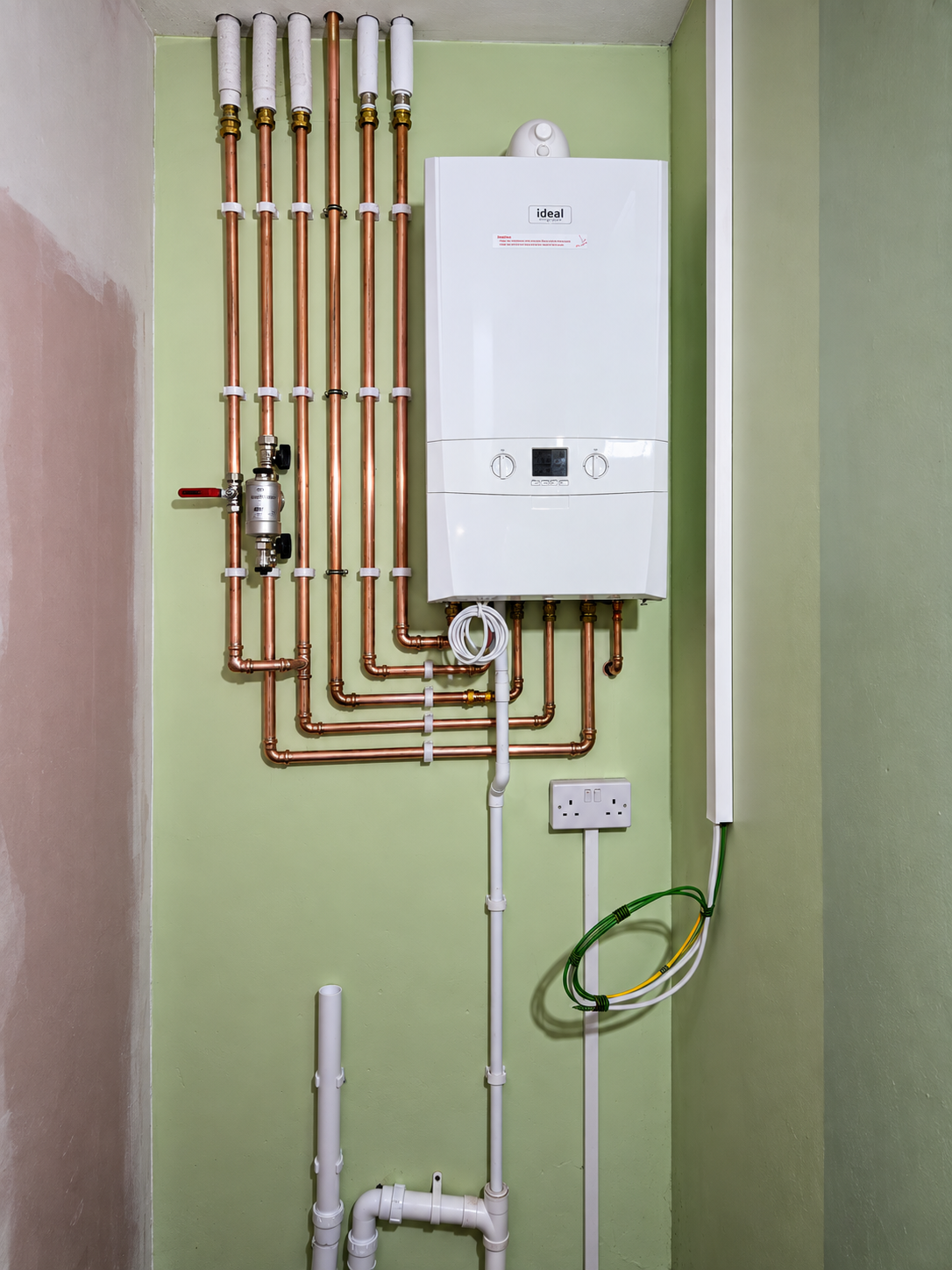 White Ideal wall-mounted boiler on a light green wall with neatly arranged copper pipework