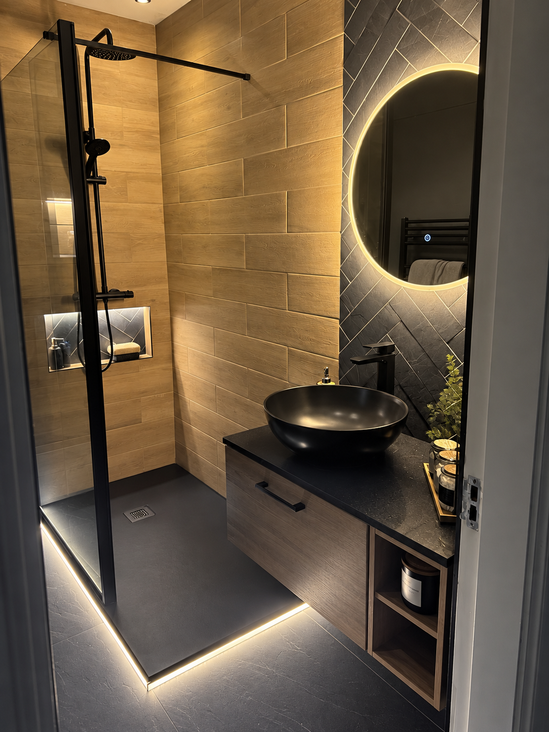 Dark bathroom with black basin, illuminated round mirror and black shower fittings